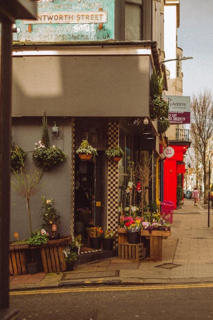 The image shows the exterior of a flower shop on Lupus Street, Pimlico, with a variety of fresh flowers arranged outside the entrance. The floral display includes vibrant pink, yellow, and purple blos