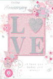 This anniversary card carries the same quiet, enduring romance you might feel wandering through Pimlico's leafy squares at dusk. At its heart, the word LOVE is beautifully embossed in raised letters, each stroke coated with a delicate dusting of blush-toned glitter edged in silver. The letters stand out from the surface with a gentle three-dimensional depth, inviting touch and adding a sense of luxury, like the satin ribbon around a carefully tied bouquet. The background is a soft, pastel pink that gradually fades into pearly white and pale grey, creating a dreamy, almost misty atmosphere that lets the central motif shine. Encircling the word LOVE, clusters of stylised flowers unfurl in blush, mauve, and soft ivory, connected by curling vines and fine, looping lines that sweep across the card like the graceful stems and foliage in a romantic arrangement. Each bloom is drawn with meticulous detail, some accented by tiny touches of silver that glint subtly, never overpowering the gentle palette. Small butterflies and swirling flourishes are tucked discreetly among the petals, adding a sense of movement and whisper-light joy, like seeing petals drift across a quiet street near St George's Square. The main greeting-On Our Anniversary and a tender line such as I love you today and always-is written in flowing script, its curves echoing the arcs of the illustrated vines. The overall impression is of a thoughtfully composed paper keepsake, softly luminous and deeply heartfelt, ideal for marking a shared journey of love in the calm, elegant surroundings of Pimlico.